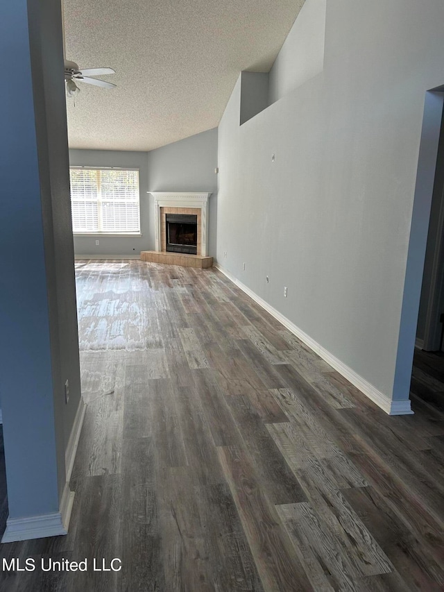 unfurnished living room with a textured ceiling, a tiled fireplace, ceiling fan, high vaulted ceiling, and dark hardwood / wood-style floors