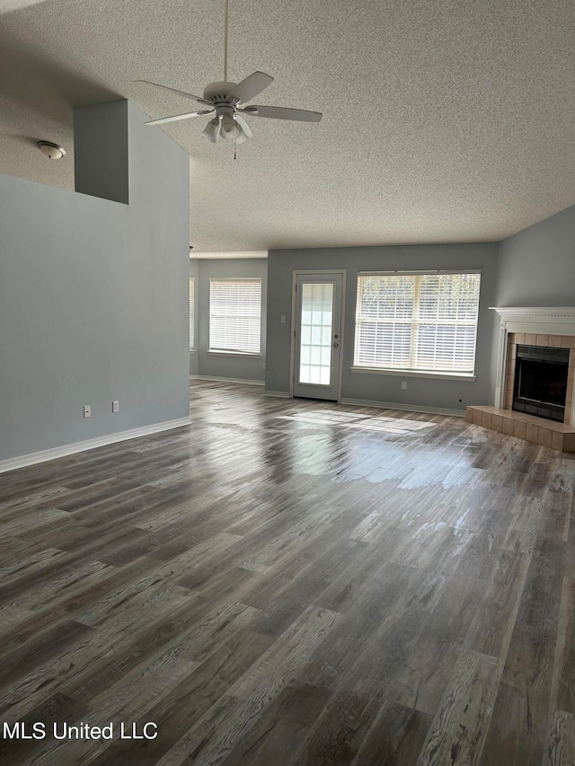 unfurnished living room featuring dark wood-type flooring, a tiled fireplace, a textured ceiling, and ceiling fan