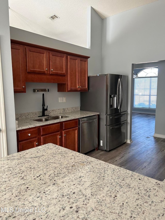 kitchen featuring a textured ceiling, light stone countertops, dark hardwood / wood-style floors, stainless steel appliances, and sink