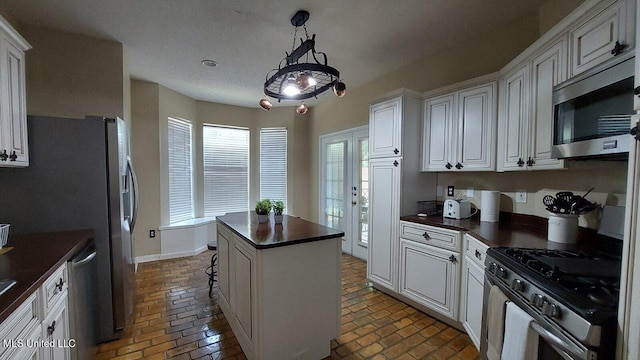 2252 Beach Dr Unit 701, Gulfport, MS 39507 - kitchen featuring appliances with stainless steel finishes, dark countertops, brick floors, a center island, and white cabinetry