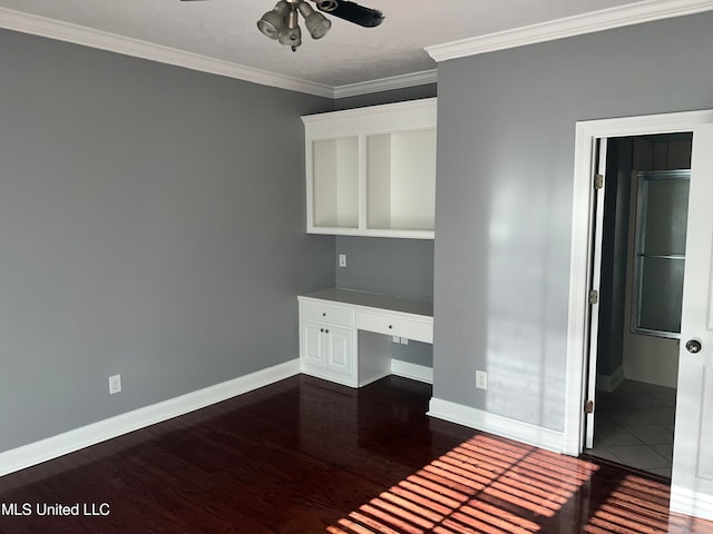 unfurnished office featuring dark hardwood / wood-style flooring, ceiling fan, built in desk, and ornamental molding