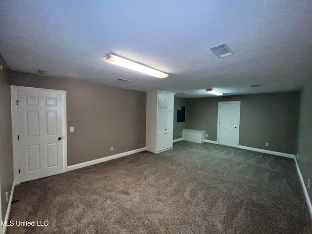 basement featuring electric panel, dark colored carpet, and a textured ceiling