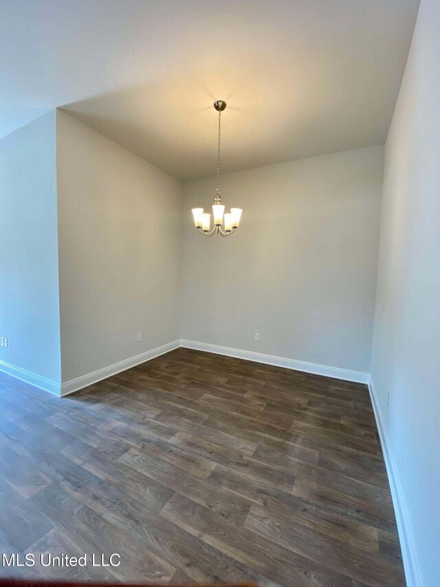 unfurnished room featuring dark wood-type flooring and a notable chandelier