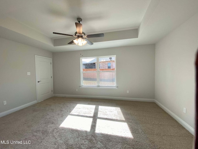 carpeted spare room with a raised ceiling and ceiling fan