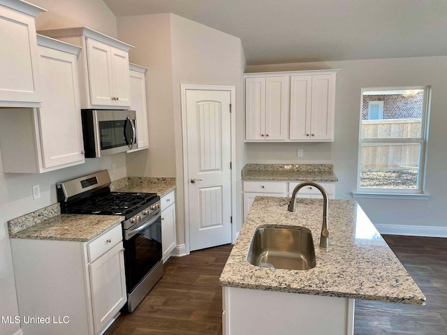 kitchen with appliances with stainless steel finishes, sink, white cabinets, a kitchen island with sink, and light stone counters