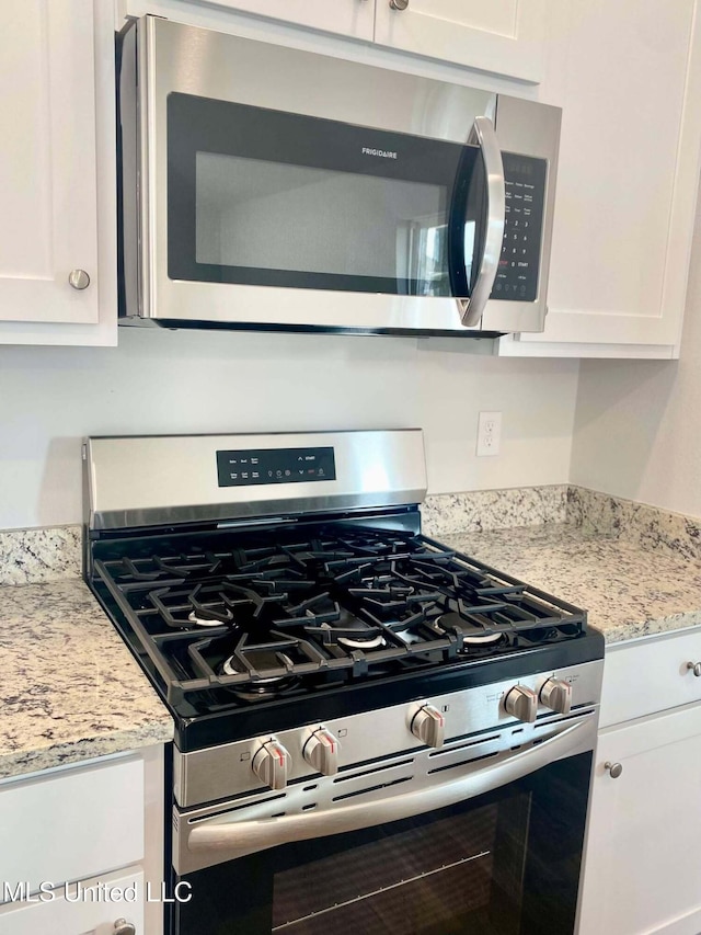 kitchen with light stone counters, stainless steel appliances, and white cabinets