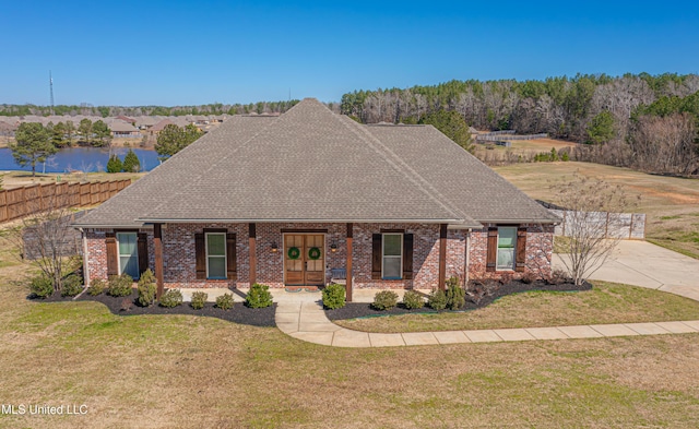 view of front facade featuring a front lawn, a shingled roof, brick siding, and a water view