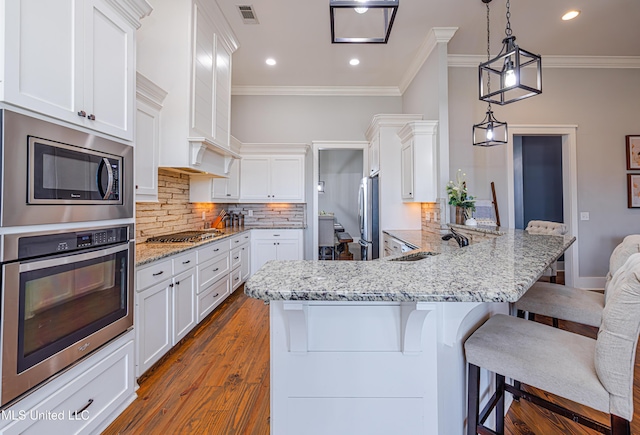 kitchen featuring visible vents, appliances with stainless steel finishes, a peninsula, white cabinetry, and a sink