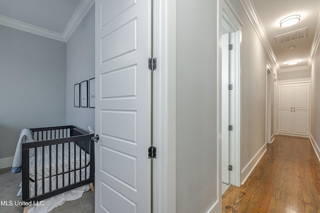 hallway with baseboards, wood finished floors, visible vents, and crown molding