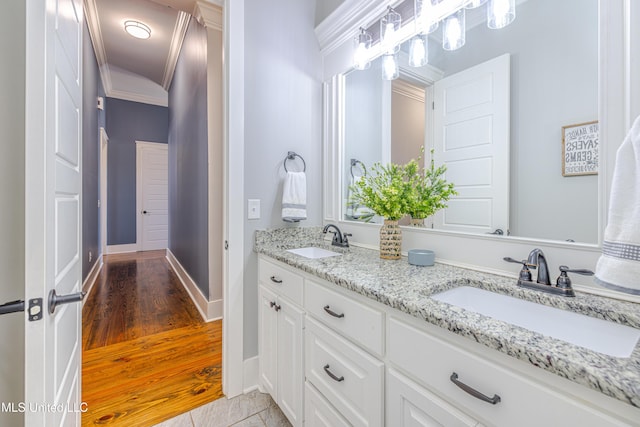 bathroom featuring double vanity, wood finished floors, a sink, and crown molding