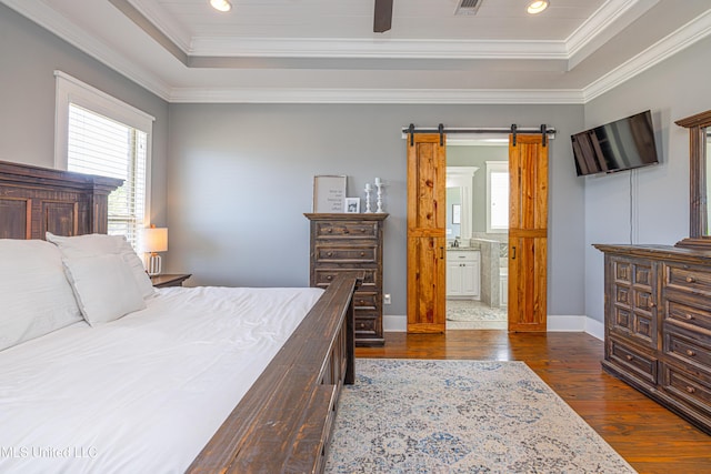 bedroom featuring dark wood-style floors, a tray ceiling, a barn door, and ornamental molding