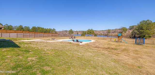 view of yard featuring a trampoline, a playground, fence, and a water view