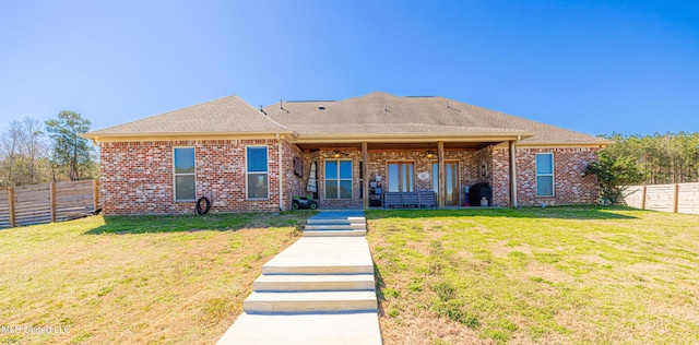 back of house featuring a yard, a fenced backyard, roof with shingles, and brick siding