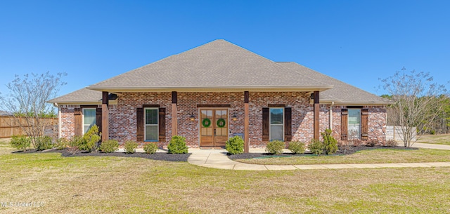 view of front of home featuring a shingled roof, a front yard, french doors, and brick siding