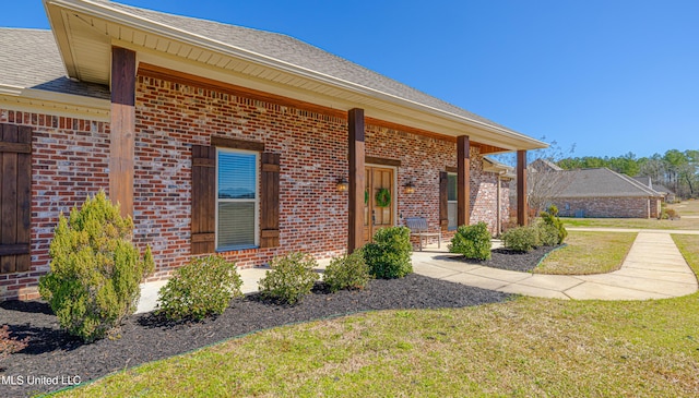 property entrance featuring roof with shingles, brick siding, and a lawn