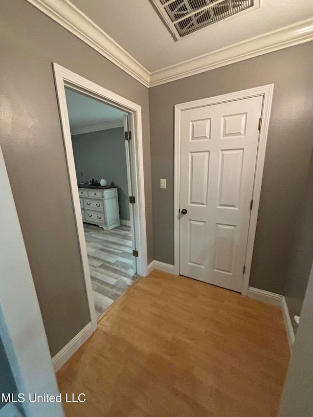 corridor with light wood-type flooring, visible vents, baseboards, and crown molding