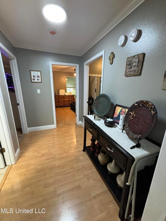 hall featuring light wood-type flooring, baseboards, and ornamental molding