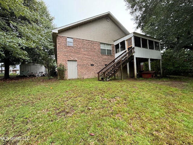 rear view of property featuring a yard, brick siding, stairs, and a sunroom