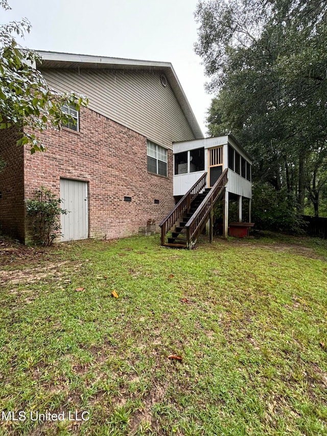 rear view of property featuring brick siding, stairway, a yard, a sunroom, and crawl space