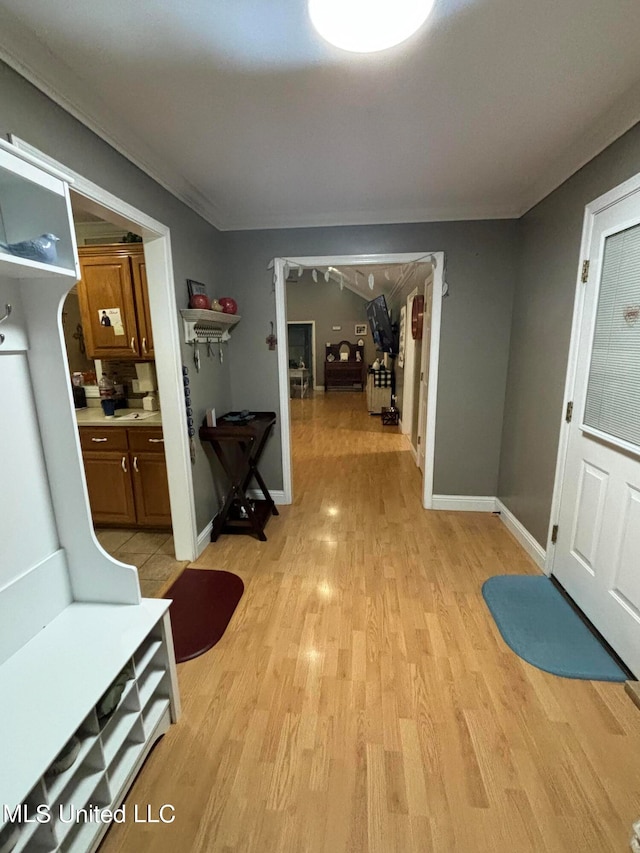 corridor with light wood-type flooring, baseboards, and crown molding