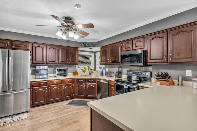 kitchen with appliances with stainless steel finishes, light countertops, ceiling fan, a sink, and ornamental molding
