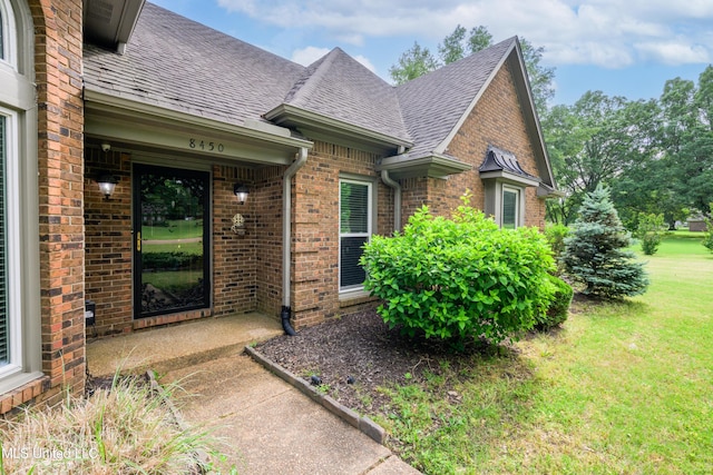 property entrance featuring brick siding, a shingled roof, and a lawn