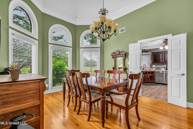 dining space featuring a towering ceiling, light wood finished floors, crown molding, a chandelier, and baseboards