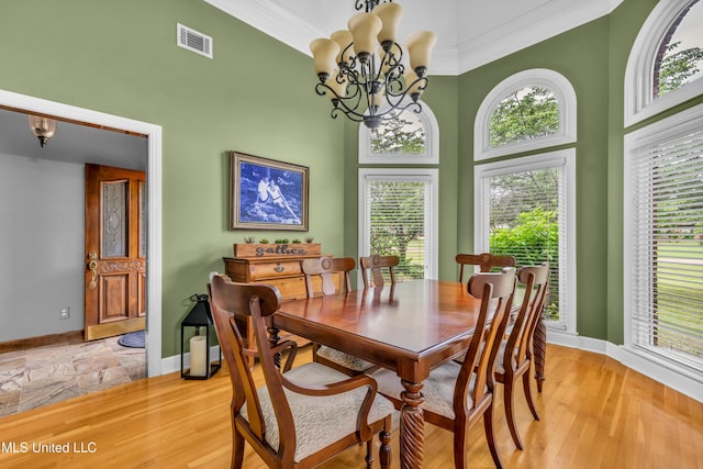 dining room featuring a chandelier, baseboards, a high ceiling, crown molding, and light wood finished floors