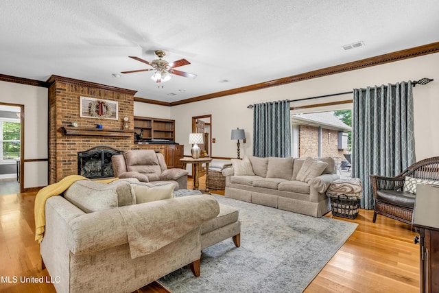 living room featuring ceiling fan, light wood-style floors, ornamental molding, a textured ceiling, and baseboards