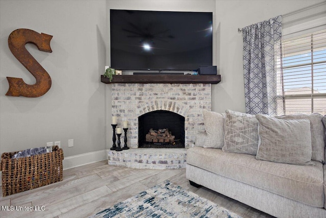 living room with a brick fireplace, baseboards, and wood finished floors