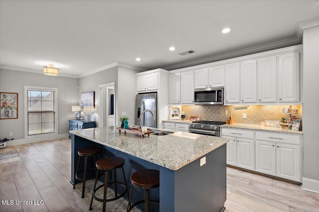 kitchen with visible vents, a breakfast bar area, stainless steel appliances, white cabinetry, and backsplash