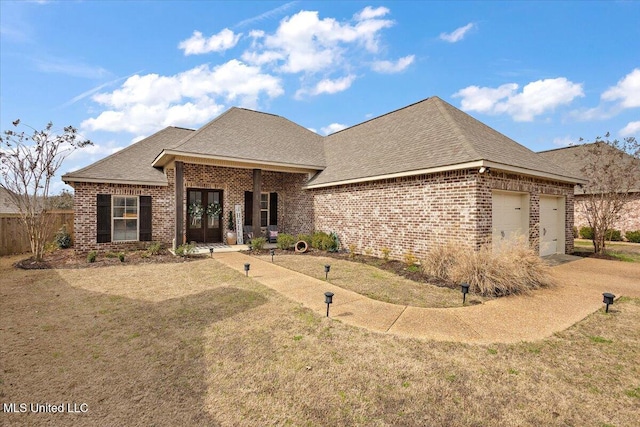 french country home featuring a garage, brick siding, french doors, roof with shingles, and a front lawn