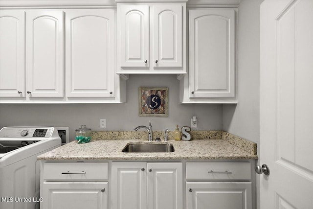 kitchen featuring washer / dryer, white cabinetry, a sink, and light stone counters