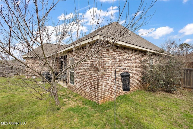 view of property exterior with brick siding, fence, and a yard