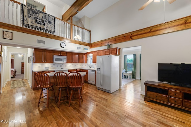 kitchen featuring ceiling fan, white appliances, light countertops, brown cabinets, and a kitchen bar