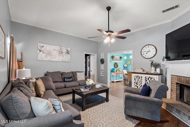 living room featuring ornamental molding, hardwood / wood-style floors, ceiling fan, and a brick fireplace