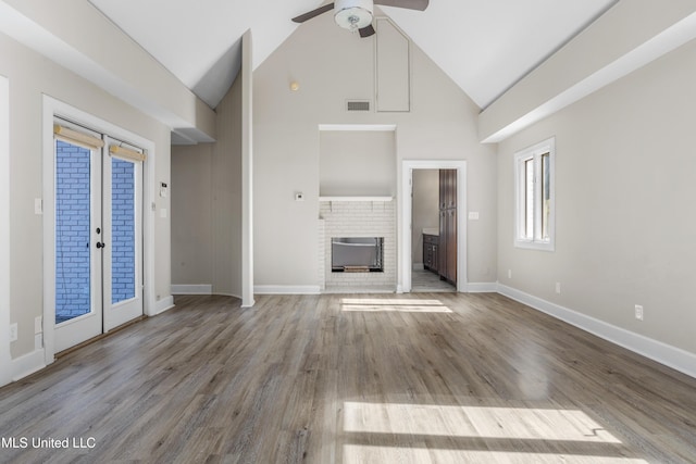 unfurnished living room featuring ceiling fan, french doors, a brick fireplace, high vaulted ceiling, and light wood-type flooring