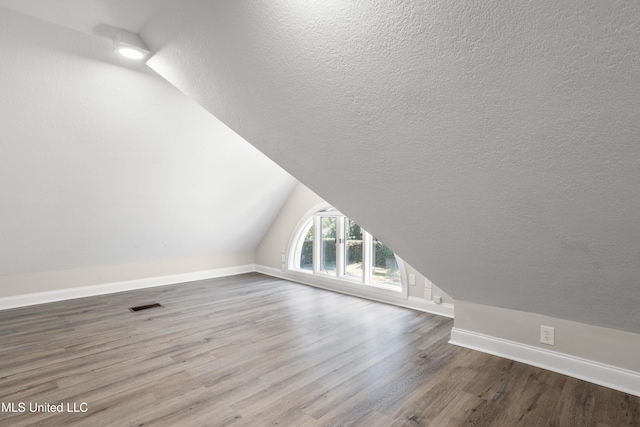 additional living space with a textured ceiling, vaulted ceiling, and hardwood / wood-style flooring