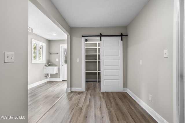 unfurnished bedroom with a walk in closet, wood-type flooring, a barn door, and sink