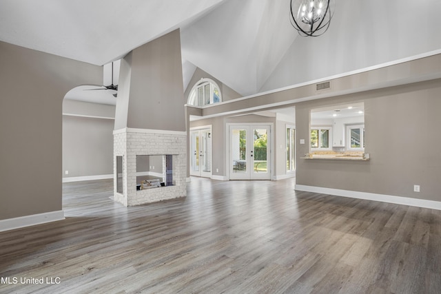 unfurnished living room with french doors, a brick fireplace, ceiling fan with notable chandelier, wood-type flooring, and high vaulted ceiling