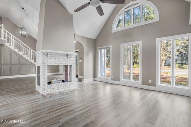 unfurnished living room with hardwood / wood-style floors, high vaulted ceiling, ceiling fan with notable chandelier, and a brick fireplace