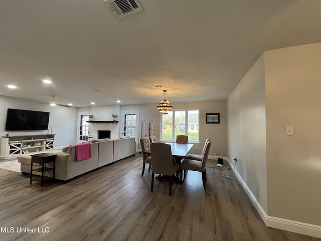 dining area with wood-type flooring, a large fireplace, and ceiling fan with notable chandelier