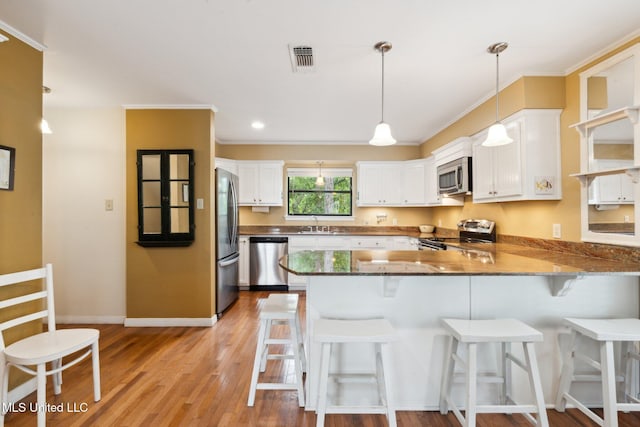 112 Dogwood Ln, Pass Christian, MS 39571 - kitchen with appliances with stainless steel finishes, a peninsula, white cabinets, light wood-type flooring, and baseboards