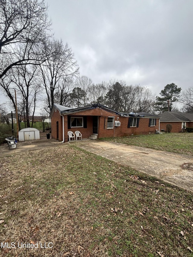 view of front facade with an outbuilding, brick siding, a front yard, a shed, and driveway