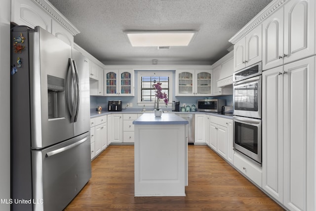 855 Dove Blvd, Bay Saint Louis, MS 39520 - kitchen featuring stainless steel appliances, glass insert cabinets, a textured ceiling, a kitchen island, and white cabinetry