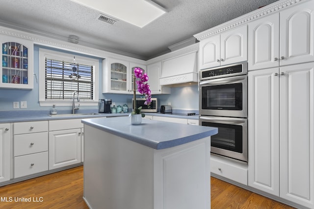 855 Dove Blvd, Bay Saint Louis, MS 39520 - kitchen with stainless steel appliances, glass insert cabinets, white cabinetry, wood finished floors, and a textured ceiling