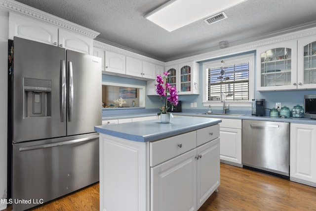 855 Dove Blvd, Bay Saint Louis, MS 39520 - kitchen with stainless steel appliances, white cabinetry, glass insert cabinets, a textured ceiling, and a center island