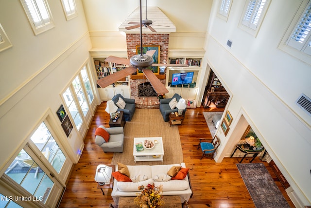 living room featuring hardwood / wood-style flooring, ceiling fan, a towering ceiling, and a fireplace