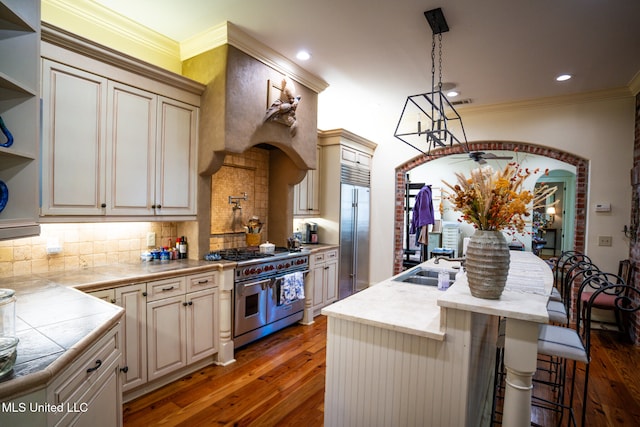 kitchen featuring dark hardwood / wood-style flooring, premium appliances, crown molding, decorative light fixtures, and a breakfast bar area