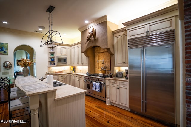 kitchen with hardwood / wood-style floors, a breakfast bar, backsplash, built in appliances, and decorative light fixtures